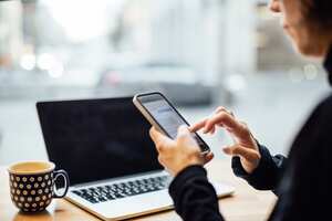 Mature businesswoman sitting at cafe and using cell phone with a laptop on table. Mid adult female texting with her smart phone at coffee shop.