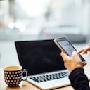Mature businesswoman sitting at cafe and using cell phone with a laptop on table. Mid adult female texting with her smart phone at coffee shop.