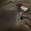 Se ve una fisura junto a una casa cubierta de ceniza en la isla canaria de La Palma, España, el miércoles 1 de diciembre de 2021. Una fisura que los vulcanólogos creen que arrojó un chorro de lava dejó un enorme agujero en el frente de la casa cuyo piso inferior estaba completamente cubierto por una montaña de ceniza. Una nueva corriente de lava del volcán en La Palma de España amenazó el miércoles con engullir una iglesia parroquial que hasta ahora ha sobrevivido a la erupción que no muestra signos de ceder en su décima semana. Foto AP / Emilio Morenatti