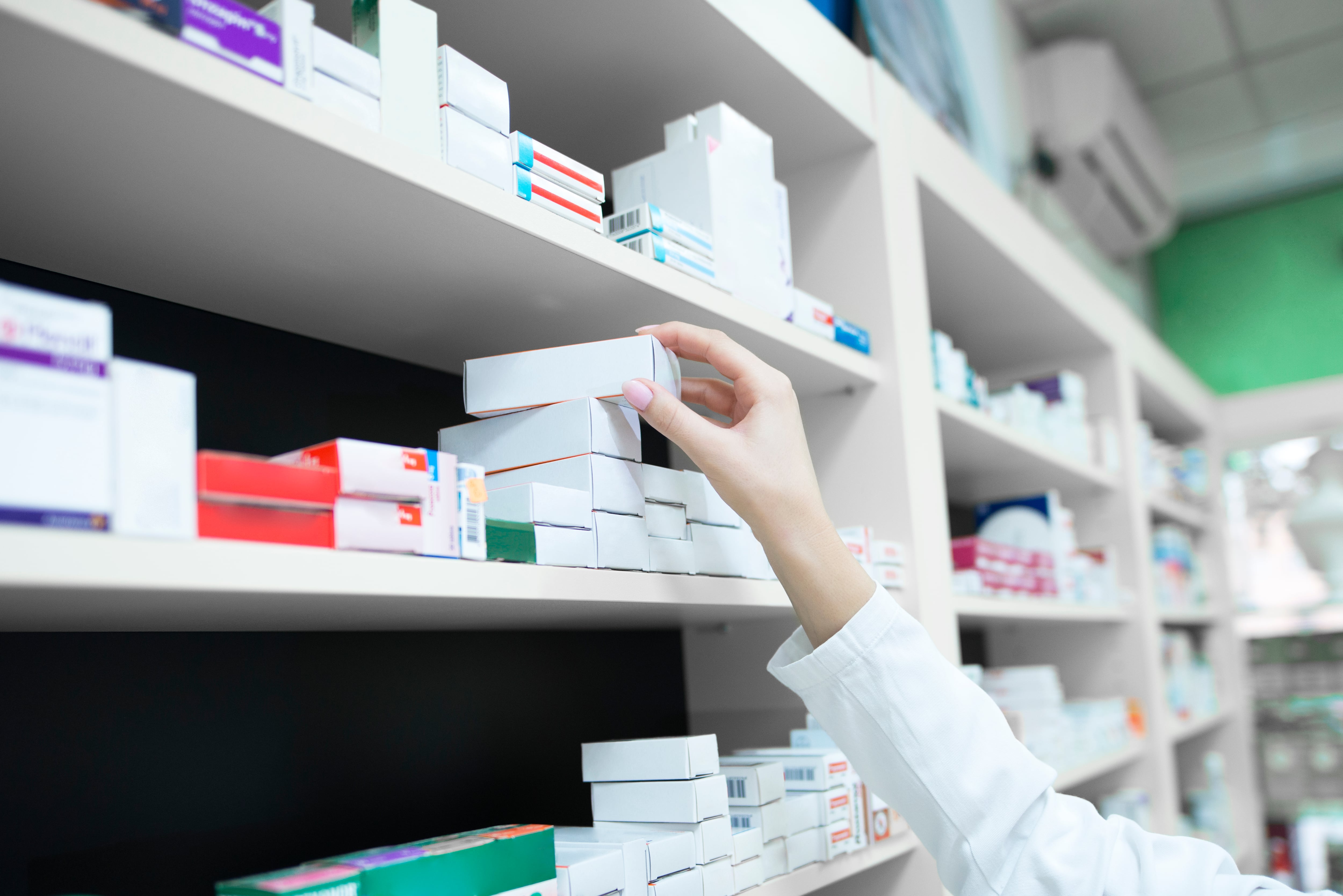 Closeup view of pharmacist hand taking medicine box from the shelf in drug store.