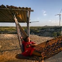 Un hombre descansa en una hamaca frente a un parque eólico en La Guajira, una imagen que refleja el encuentro entre el territorio, las comunidades y los nuevos proyectos de energías renovables en Colombia.