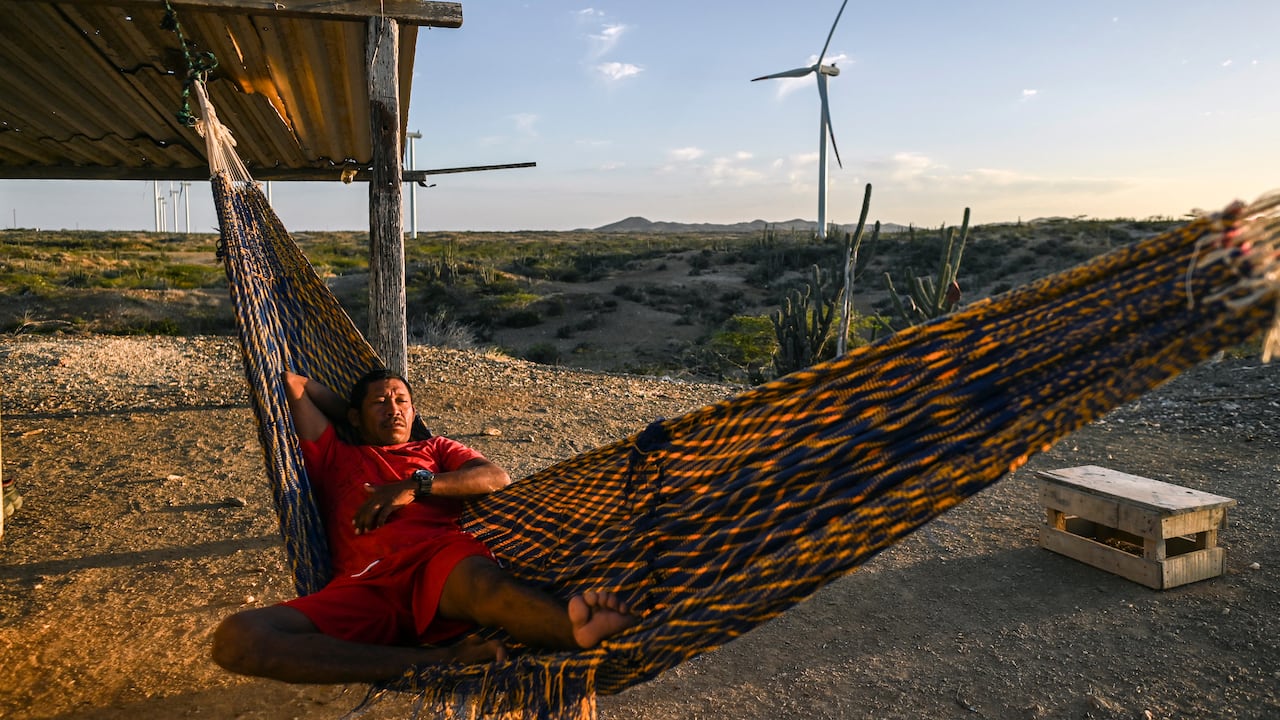 Un hombre descansa en una hamaca frente a un parque eólico en La Guajira, una imagen que refleja el encuentro entre el territorio, las comunidades y los nuevos proyectos de energías renovables en Colombia.