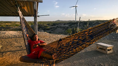 Un hombre descansa en una hamaca frente a un parque eólico en La Guajira, una imagen que refleja el encuentro entre el territorio, las comunidades y los nuevos proyectos de energías renovables en Colombia.