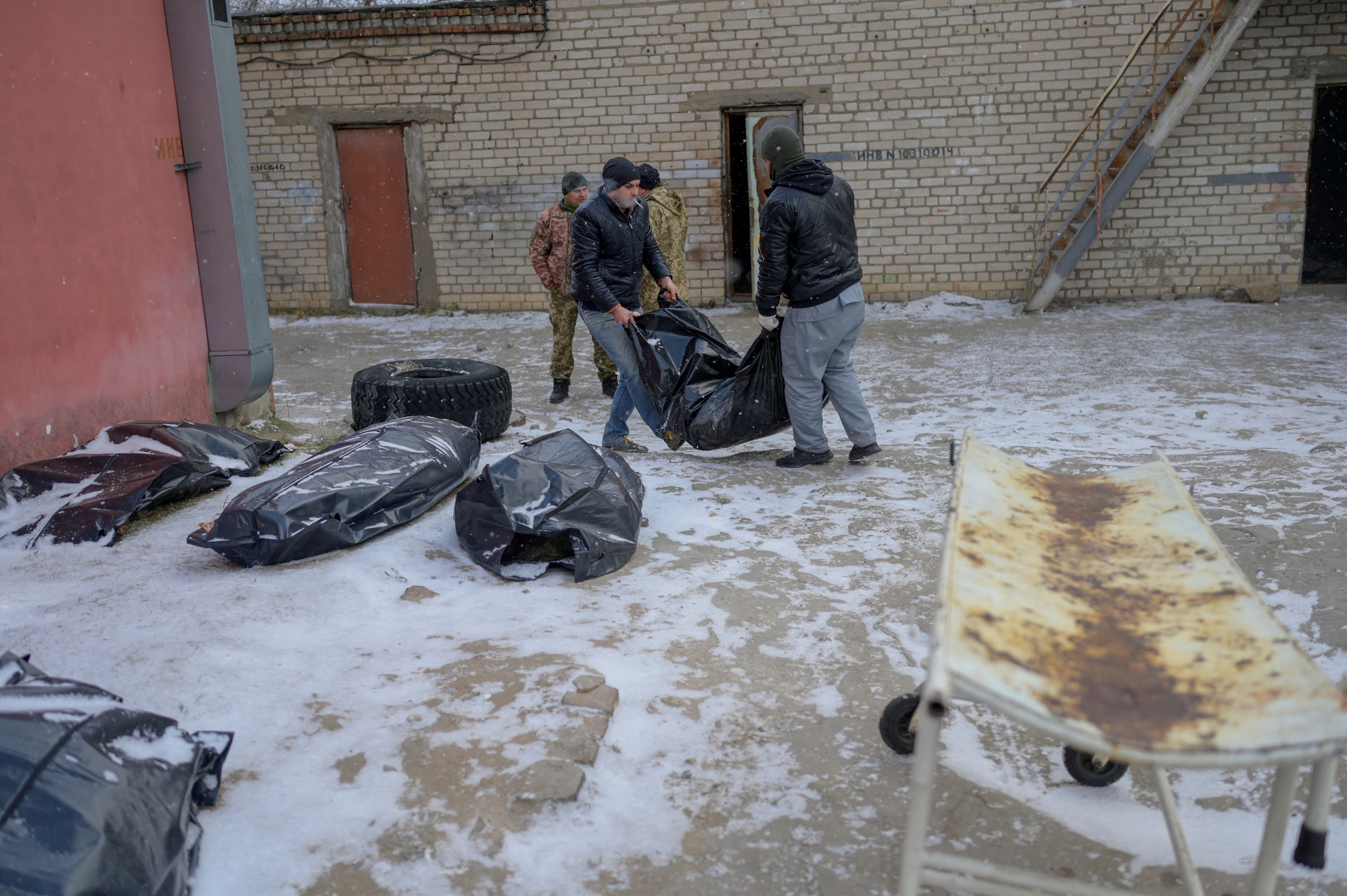 Dos hombres cargan un cuerpo en una bolsa para cadáveres para colocarlo junto a otros en un patio cubierto de nieve de una morgue en Mykolaiv, una ciudad a orillas del Mar Negro que ha estado bajo ataque ruso durante días el 11 de marzo de 2022. - El cadáver yace con las manos entrelazadas, como en oración. De hecho, dice el empleado de la morgue, estaba lanzando cócteles molotov cuando los rusos lo atraparon. Le ataron las manos y lo ejecutaron. Tales son las escalofriantes imágenes de la morgue de Mykolaiv, una ciudad a orillas del Mar Negro que ha enfrentado días de ataque ruso. Afuera, en el patio del instituto forense donde se encuentra la morgue, la nieve cae constantemente sobre cadáveres envueltos en bolsas de plástico gris, que esperan ser evacuados. (Foto por BULENT KILI
