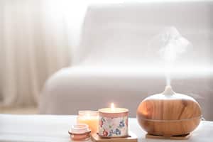 Modern oil aroma diffuser in the living room on the table with burning candles . The concept of refreshing and purifying the air in the house.