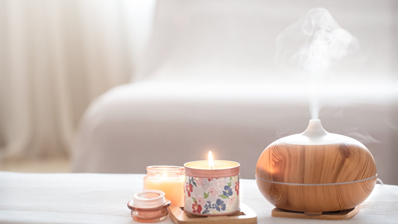 Modern oil aroma diffuser in the living room on the table with burning candles . The concept of refreshing and purifying the air in the house.