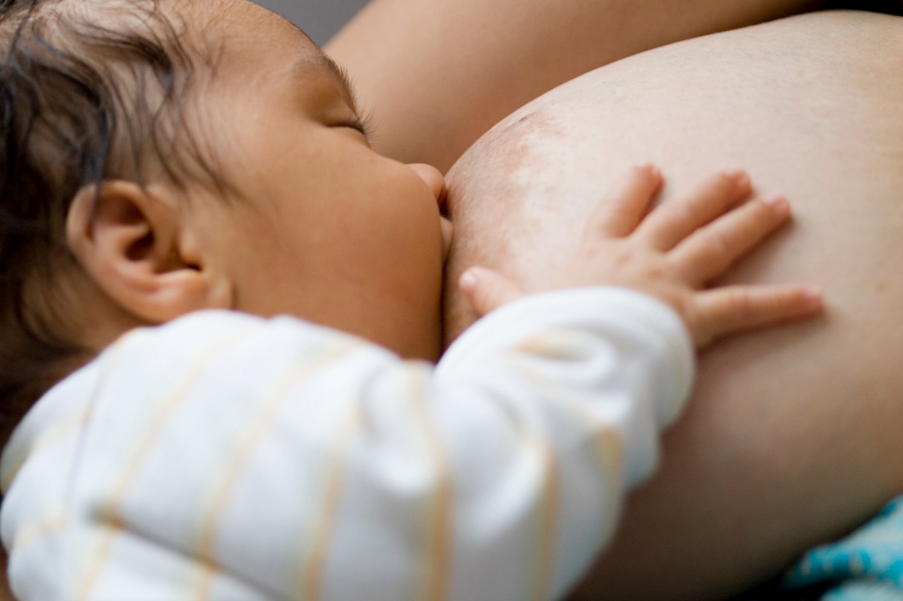 Royalty free stock photo of 3 month old baby who is being breastfed. She has her eyes closed with her right hand open. It shows a very close relationship between the baby and the mother.