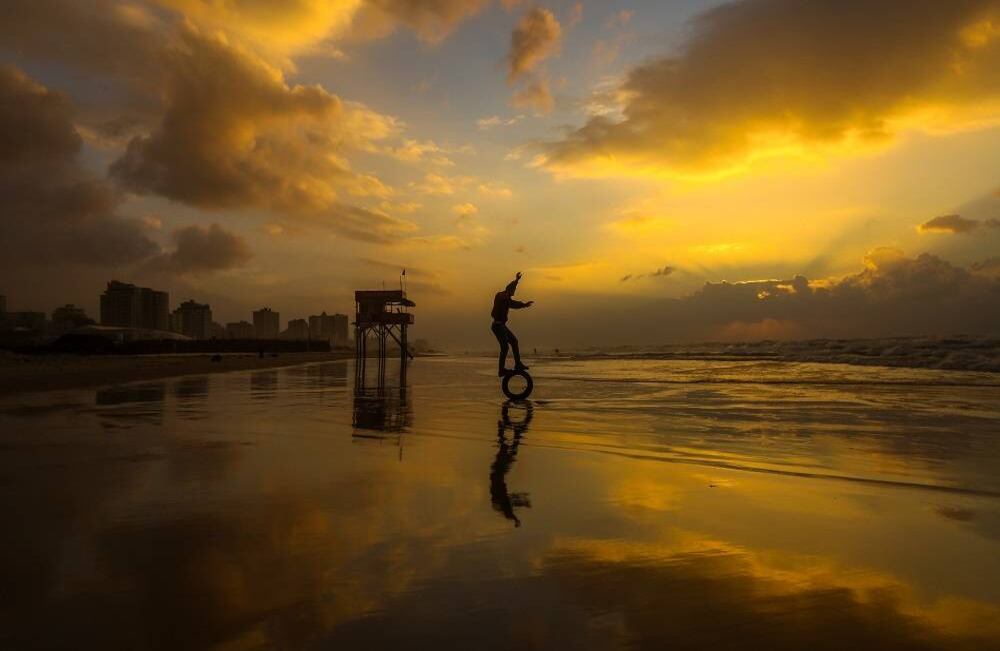 Un joven palestino intenta equilibrar un neumático en la playa al atardecer en la ciudad de Gaza el 24 de diciembre de 2017. Foto: AFP / MAHMUD HAMS