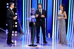 El ex futbolista Gianluigi Buffon habla con la anfitriona Esther Sedlaczek, a la derecha, y Pedro Pinto a la izquierda junto al trofeo de la Eurocopa 2024 durante el sorteo de la final del torneo de fútbol de la UEFA Euro 2024 en la sala de conciertos Elbphilharmonie en Hamburgo, Alemania, el sábado 2 de diciembre. 2023. (Foto AP/Martin Meissner)