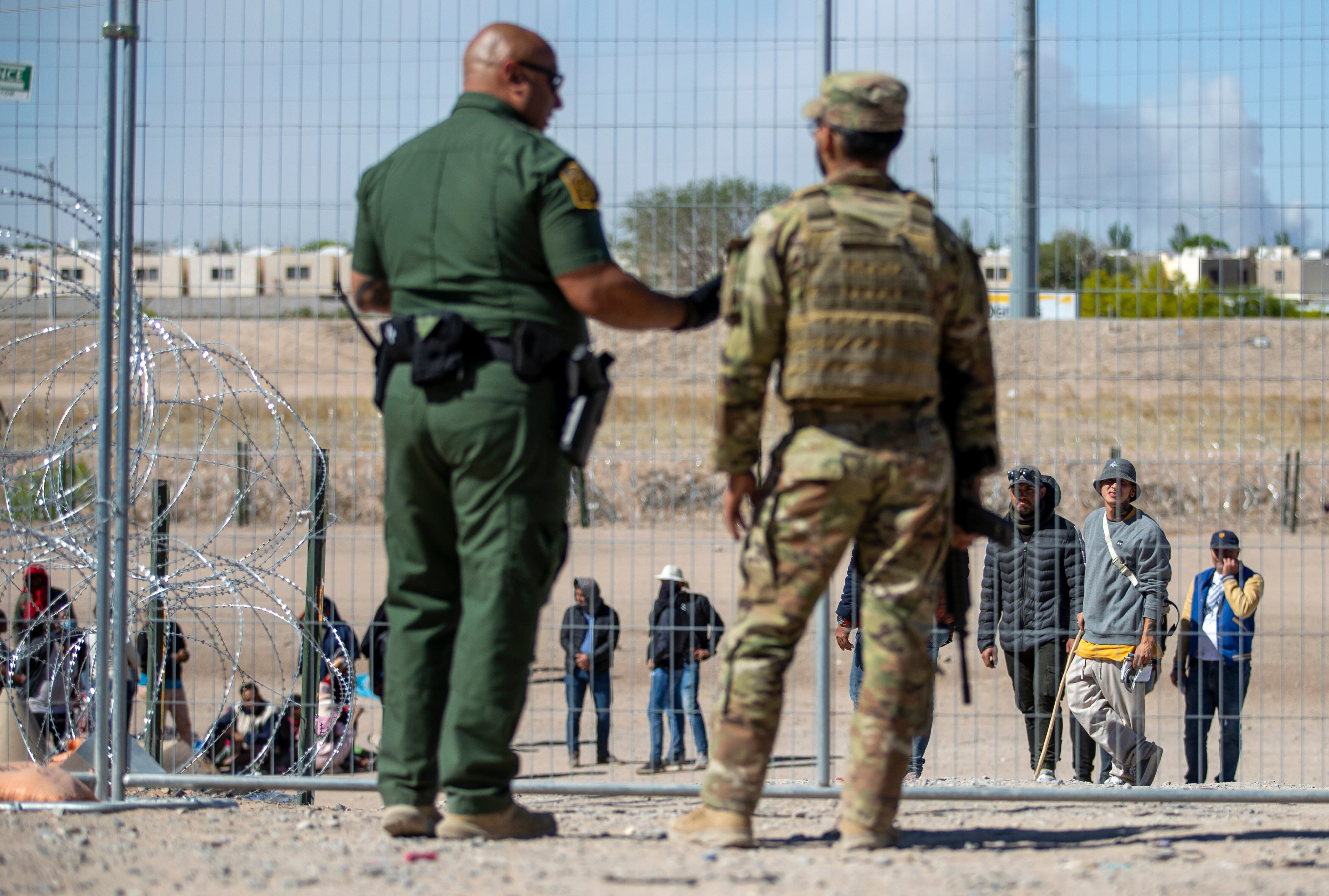 Migrantes aguardan a un costado del muro fronterizo vigilado por la Patrulla Fronteriza y la Guardia Nacional de Texas el miércoles 10 de mayo de 2023, con el fin de ingresar a El Paso, Texas. A partir del jueves, el gobierno del presidente Joe Biden comenzará a negarle el asilo a los migrantes que se presenten en la frontera con México sin primero haber presentado una solicitud en línea o pedido protección en el país por el que pasaron