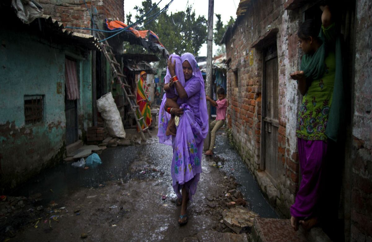 Una mujer de la India carga su hijo en brazos mientras corre por las calles de Nueva Dehli. La única protección que tiene frente a la lluvia es su sari. (AP)