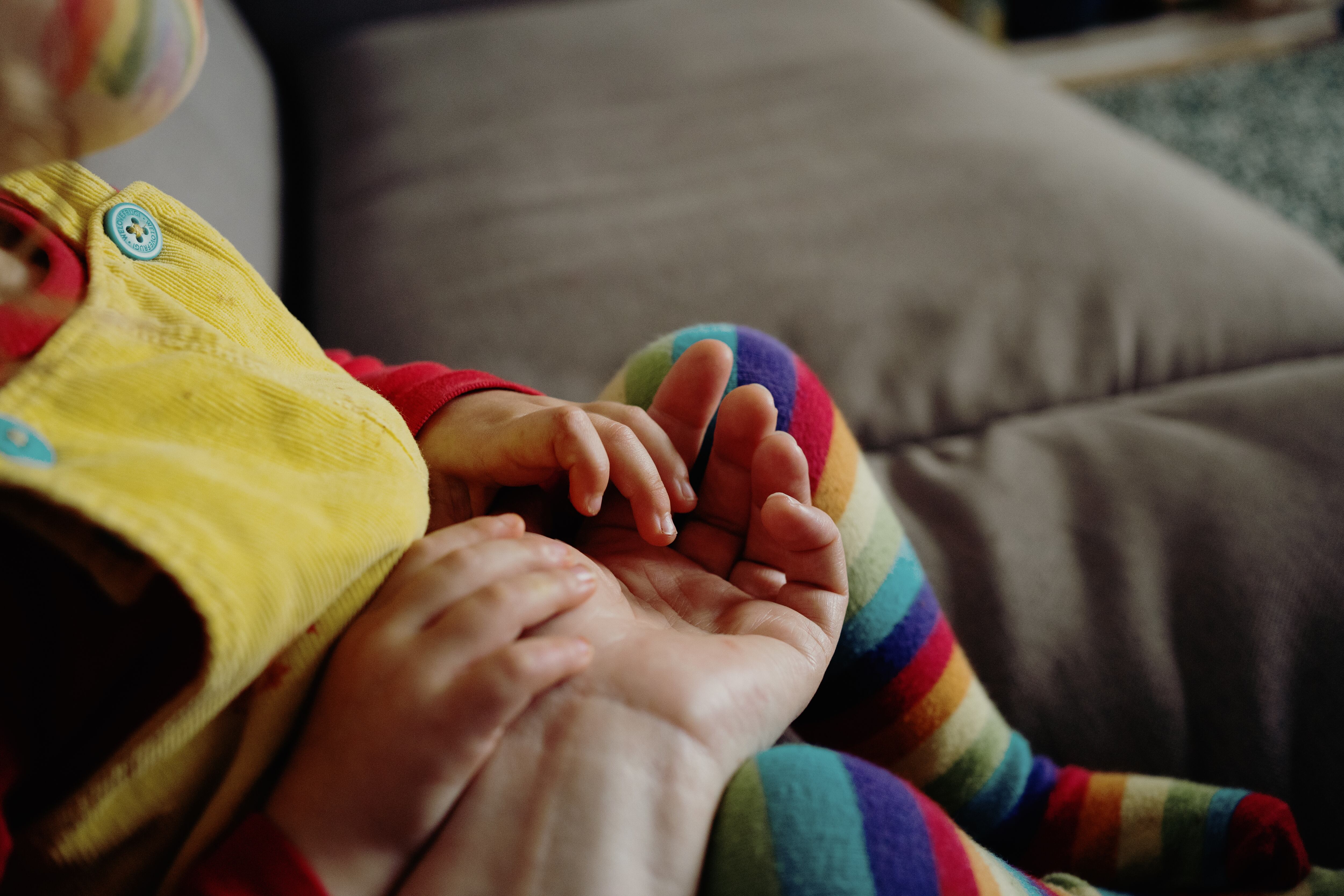 Niño pequeño sobre las piernas de su cuidador o padre usando medias de colores como el arcoiris y la bandera LBTIQ