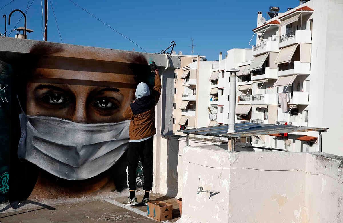 S.F., un grafitero griego de 16 años, pinta en aerosol a una mujer con una máscara facial, en el techo de su bloque de apartamentos, en Atenas. Grecia ha impuesto una amplia gama de medidas de seguridad pública para tratar de contener el brote de coronavirus, incluidos los cierres de escuelas y tiendas. Foto: Thanassis Stavrakis/ AP.