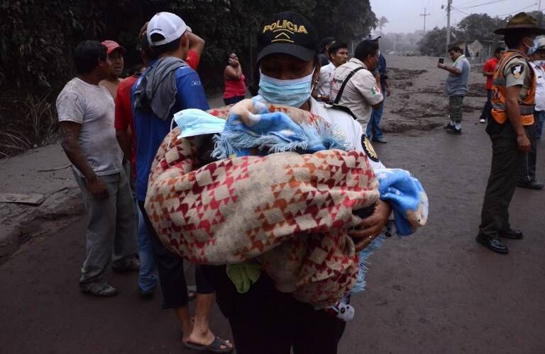 Un oficial de policía carga a un bebé después de la erupción del volcán Fuego, en el pueblo de El Rodeo, departamento de Escuintla, a 35 km al sur de Ciudad de Guatemala. AFP