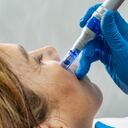 Primer plano de una mano con guantes azules usando un bolígrafo con microagujas en la cara de una mujer mayor durante un tratamiento cosmético, imagen de referencia