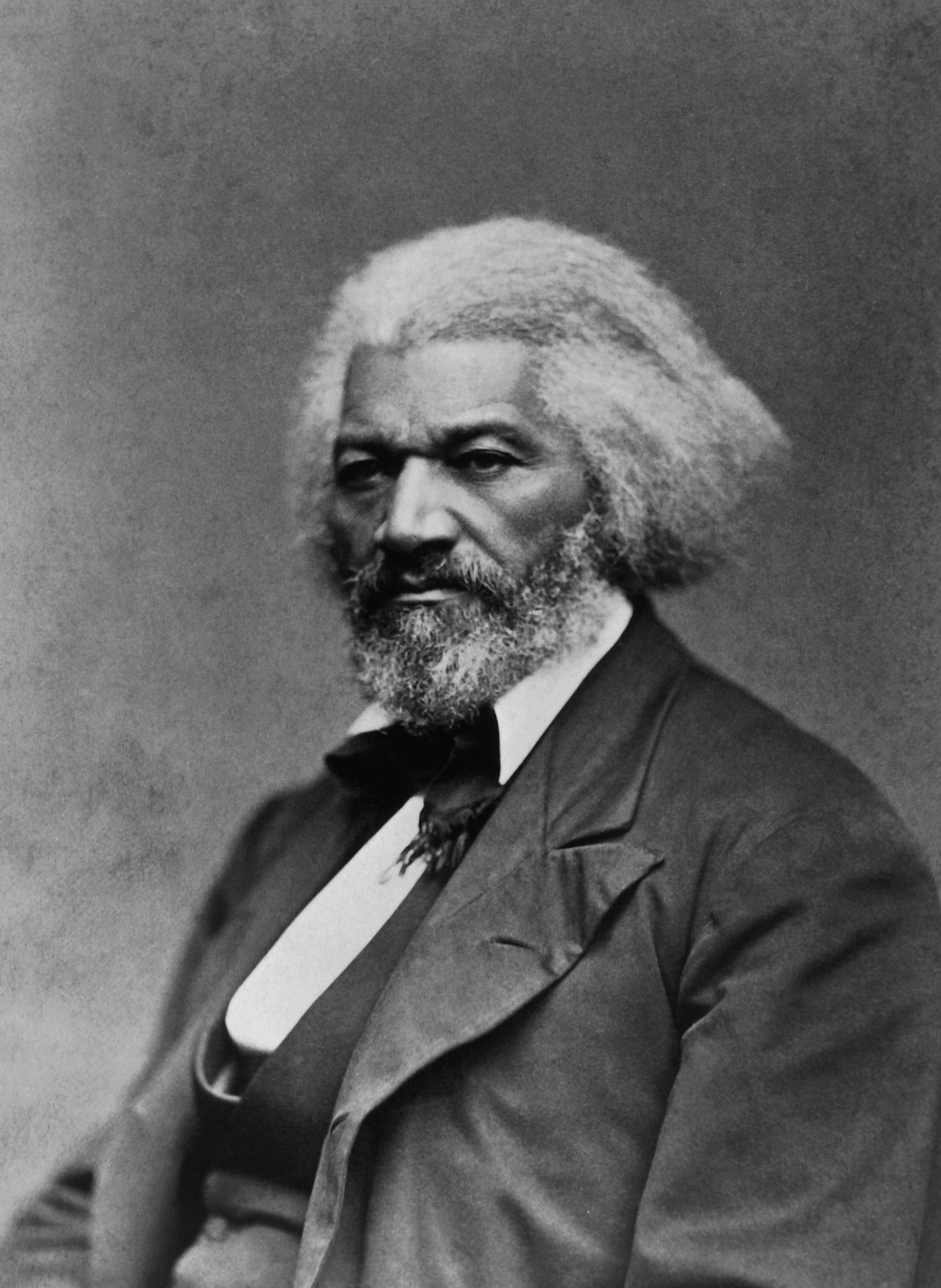 Retrato en blanco y negro de Frederick Douglass, con cabello canoso y barba, vistiendo traje formal y mirada firme.
