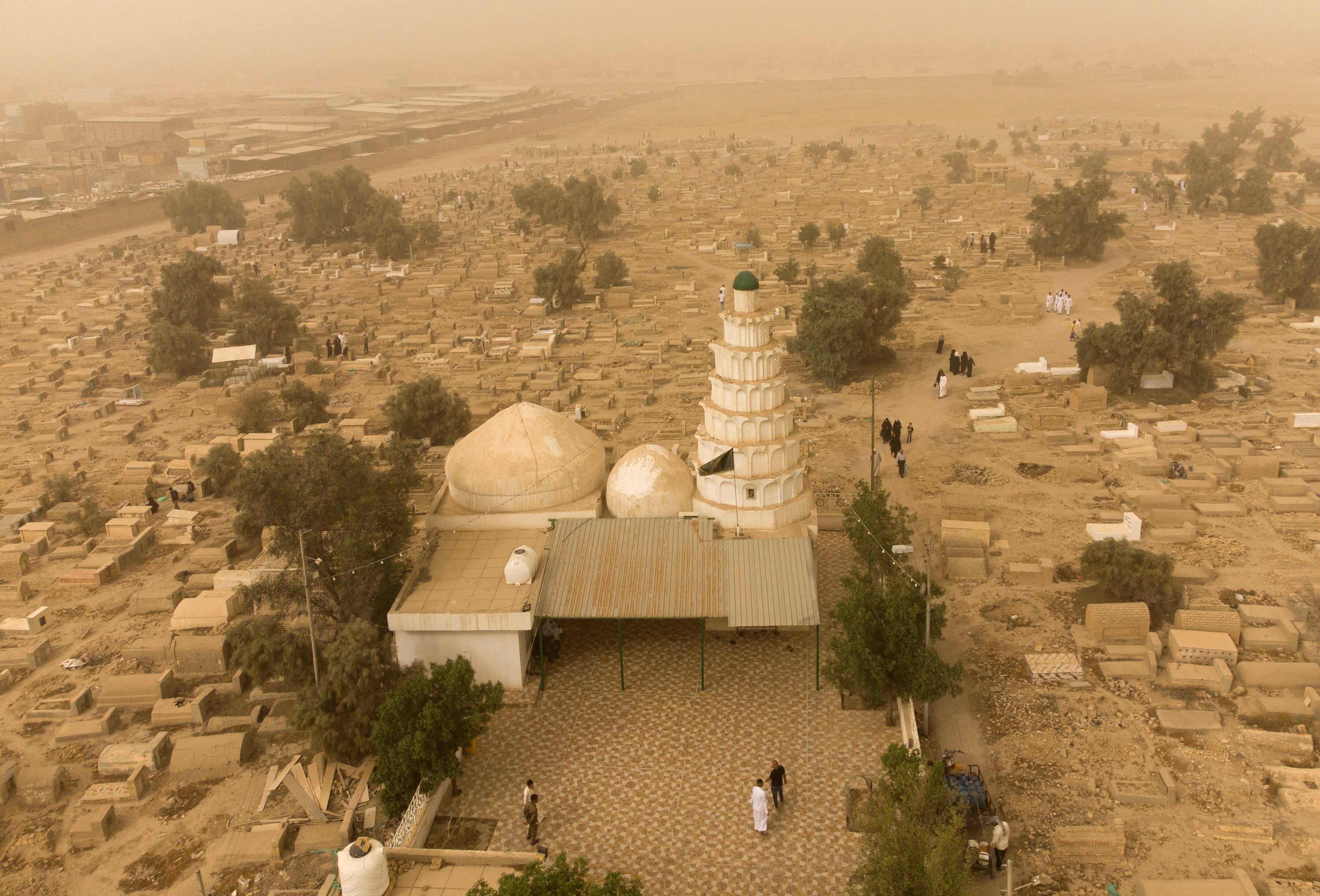 Una vista aérea muestra a musulmanes iraquíes visitando las tumbas de sus familiares durante una tormenta de polvo el primer día de Eid al-Fitr en el cementerio de Hassan al-Basri en el distrito de Zubayr de la gobernación de Basora, en el sur de Irak, el 2 de mayo de 2022. (Foto por Hussein Faleh / AFP)