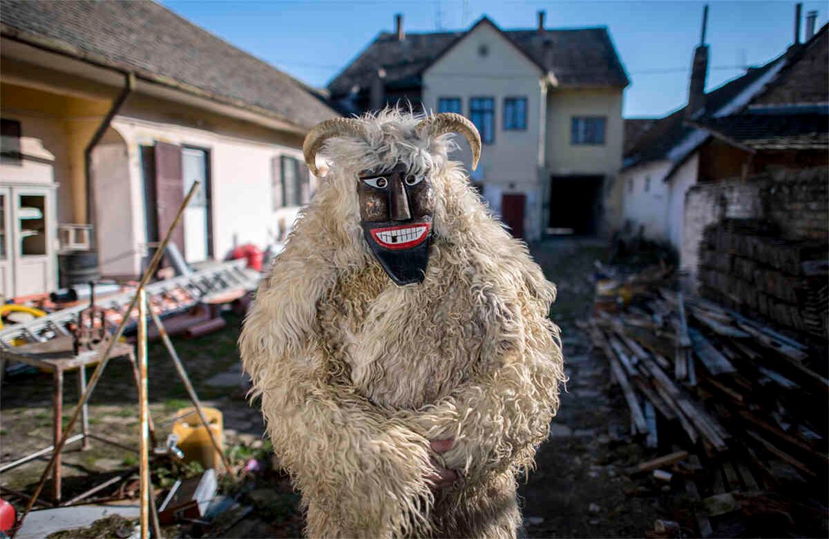 Un hombre con una máscara y un disfraz de piel de oveja está en un patio en Mohacs, Hungría, el jueves 20 de febrero de 2020. El tradicional carnaval de Busho marca el final del invierno que se remonta al siglo XVI, cuando los miembros del grupo étnico croata Shokatz vestían con trajes similares y espantosas máscaras de madera para ahuyentar a los invasores. Foto: Tamas Soki /MTI vía AP. 