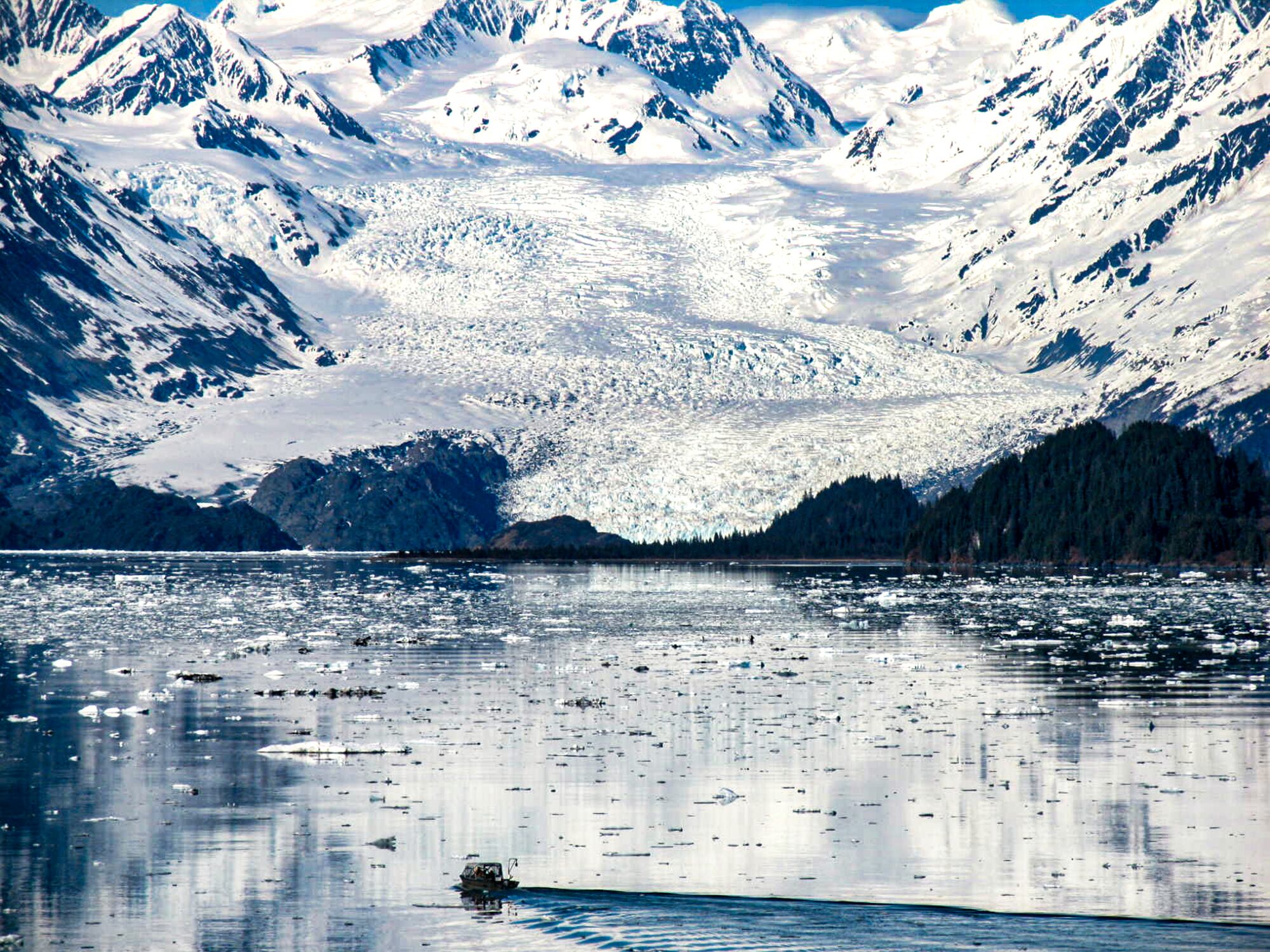 Glacier bay Alaska mirror reflection at Johns Hopkins Glacier, we see a beautiful mirror like reflection over the water from the glacier above the water, there is a small boat going toward the glacier, the shoot was taken from a cruise ship, this is why the shot has a higher position as high angle shot and this is why we see a high volume reflection over the water bed.