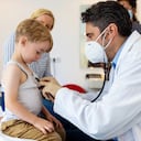 Doctor con mascarilla comprobando a un niño pequeño en su clínica. Pediatra examina al paciente niño con estetoscopio en la clínica. Covid