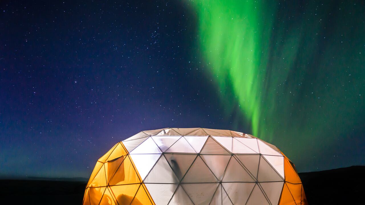 Carpa domo iluminada con aurora boreal en el fondo, en Narsaq Vestgronland, un lugar ubicado en Groenlandia