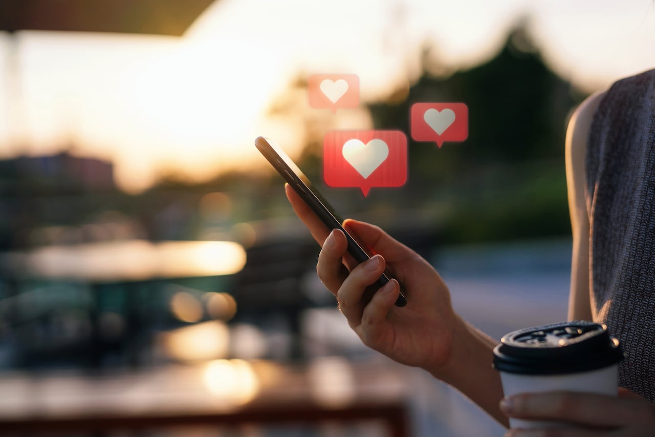 Primer plano de una joven que revisa la red social en un teléfono inteligente mientras viaja por la ciudad. Teléfono móvil con mensaje de burbuja de discurso emoji de corazón en la pantalla.