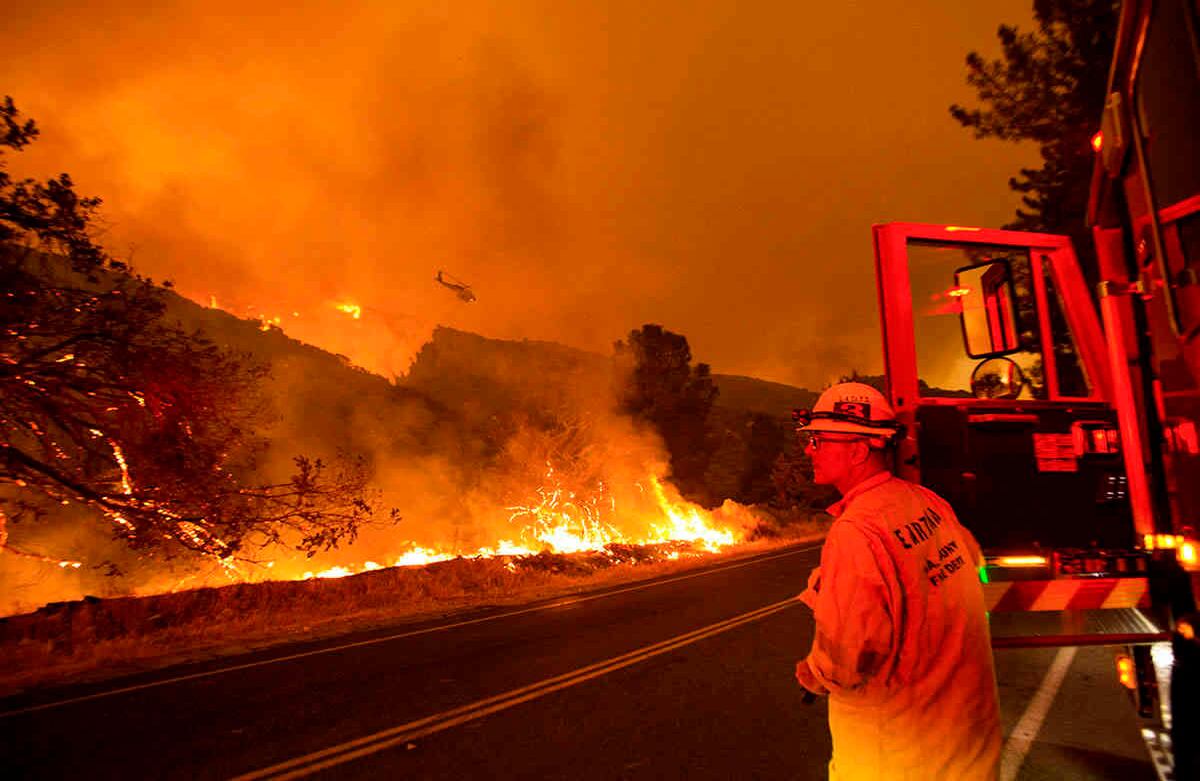 Un bombero observa cómo un helicóptero arroja agua sobre el incendio del lago Hughes en el Bosque Nacional Ángeles, el miércoles 12 de agosto de 2020, al norte de Santa Clarita, California. Foto: Ringo H.W. Chiu / AP   