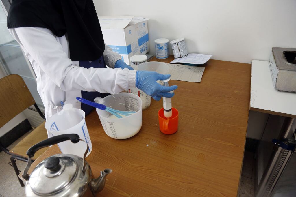 Un funcionario de salud prepara fórmula infantil mientras niños yemeníes reciben tratamiento contra la desnutrición con recursos limitados en la Unidad de Lucha contra la Desnutrición del Hospital Sabeen en Sanaa, Yemen, el 17 de abril de 2022 (Foto de Mohammed Hamoud/Agencia Anadolu vía Getty Images)