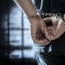 Arrested man in handcuffs with handcuffed hands behind back in prison