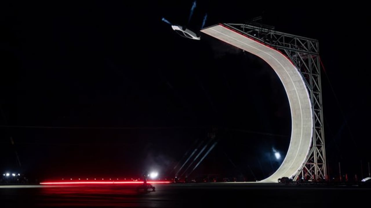 El Tesla Roadster realizando un salto acrobático tras despegar de una estructura metálica curva iluminada durante su presentación.
