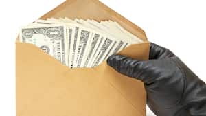 Persona con guantes de cuero negro sosteniendo un sobre marrón lleno de billetes de dólar. Aislado en un fondo blanco.