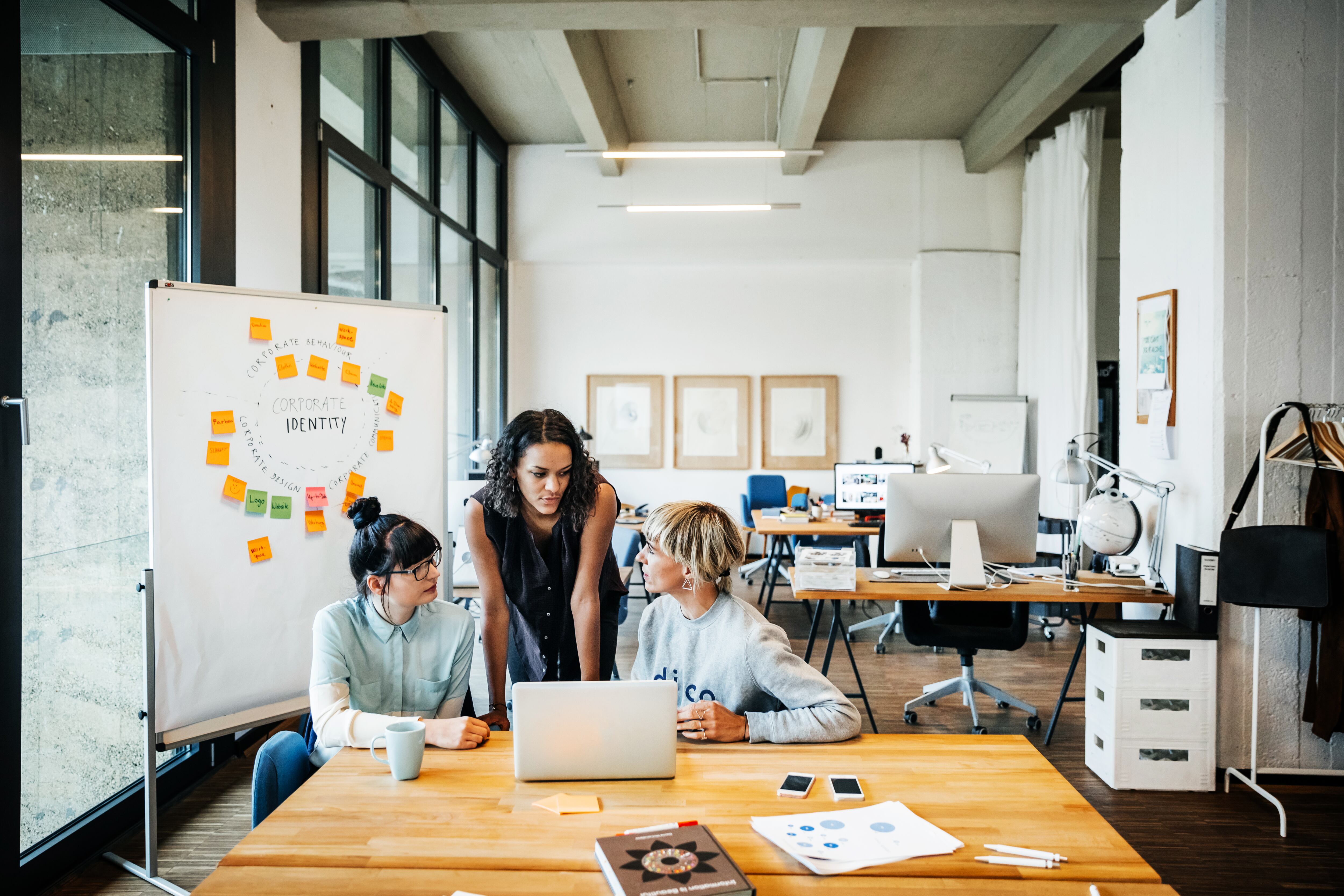 Tres mujeres empresarias jóvenes casuales que tienen una reunión con un portátil en un loft de oficina moderno.