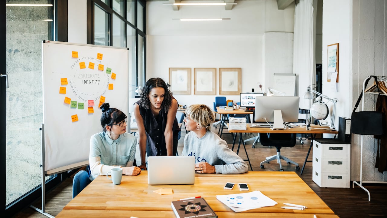 Tres mujeres empresarias jóvenes casuales que tienen una reunión con un portátil en un loft de oficina moderno