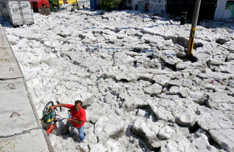 Un hombre con una bicicleta camina sobre el granizo en la zona este de Guadalajara, Estado de Jalisco, México, el 30 de junio de 2019. La acumulación de granizo en las calles de Guadalajara enterró vehículos y dañó casas. (Foto por ULISES RUIZ / AFP)