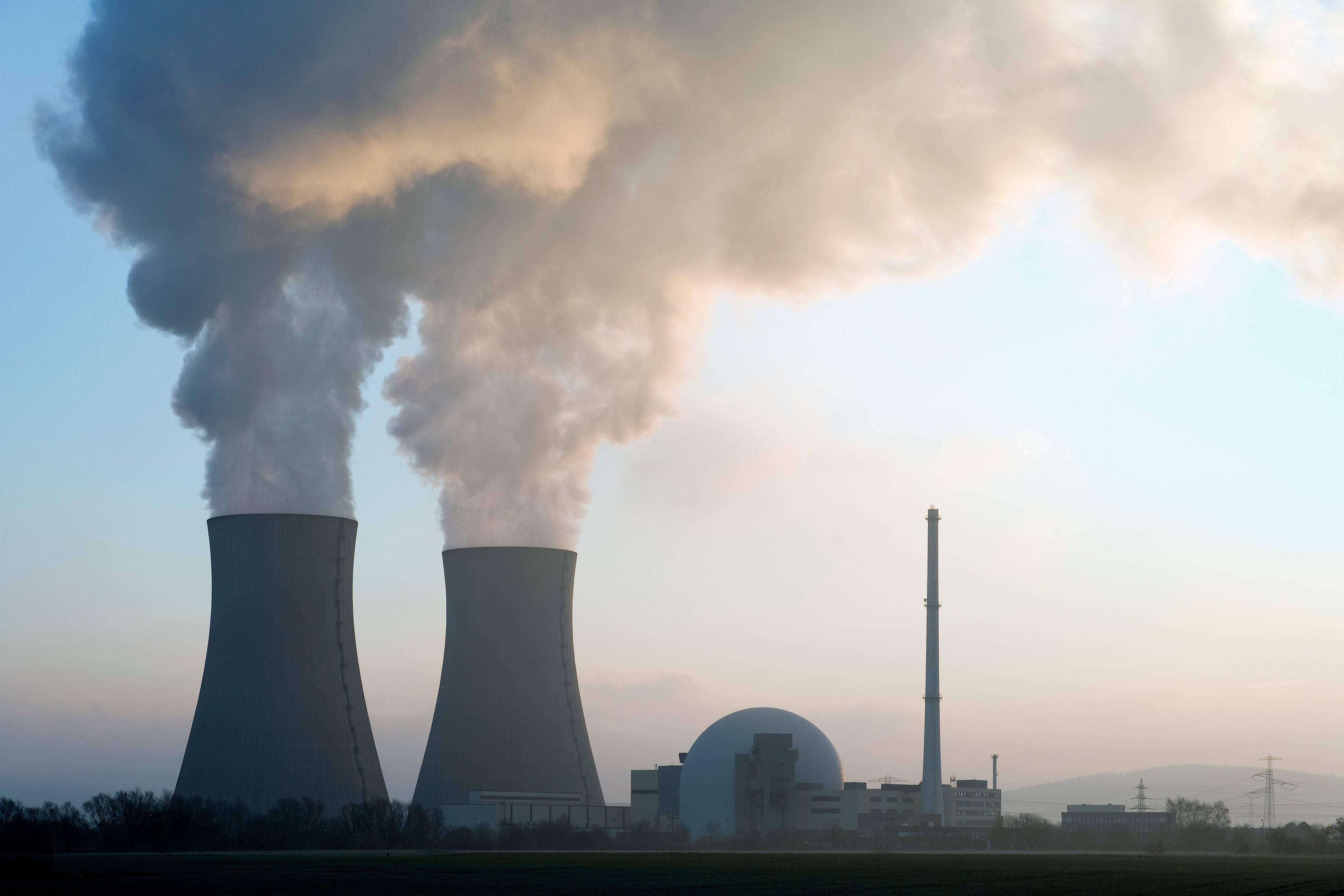 Central nuclear con torres de enfriamiento humeantes al amanecer. Imagen de referencia