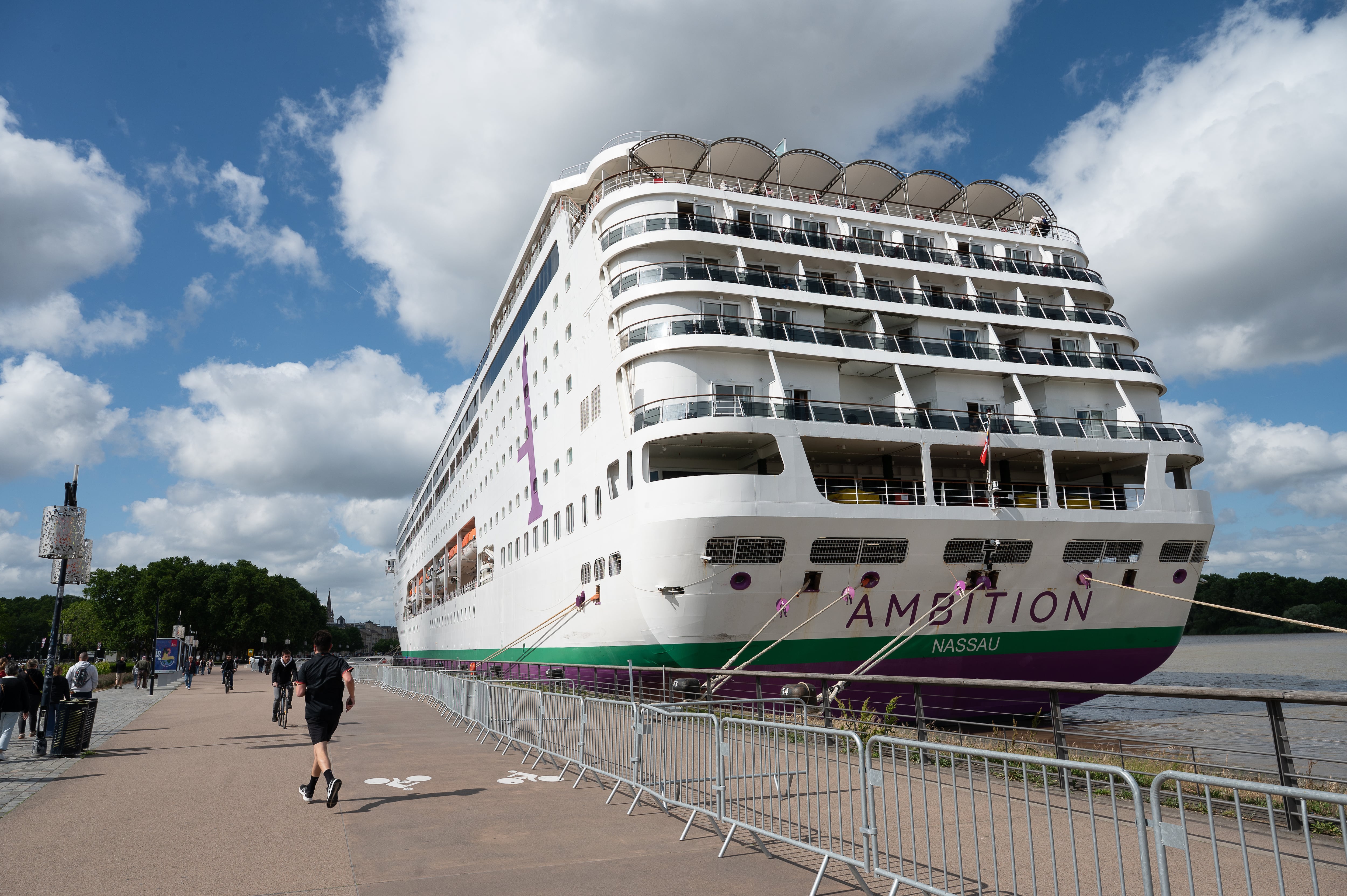 La gente pasa junto al crucero británico Ambition, mientras las autoridades francesas ordenaron a 1.700 pasajeros y tripulantes permanecer a bordo debido a un brote de enfermedad gastrointestinal, en Burdeos, suroeste de Francia, el miércoles 13 de mayo de 2026. (Foto AP/Caroline Blumberg)