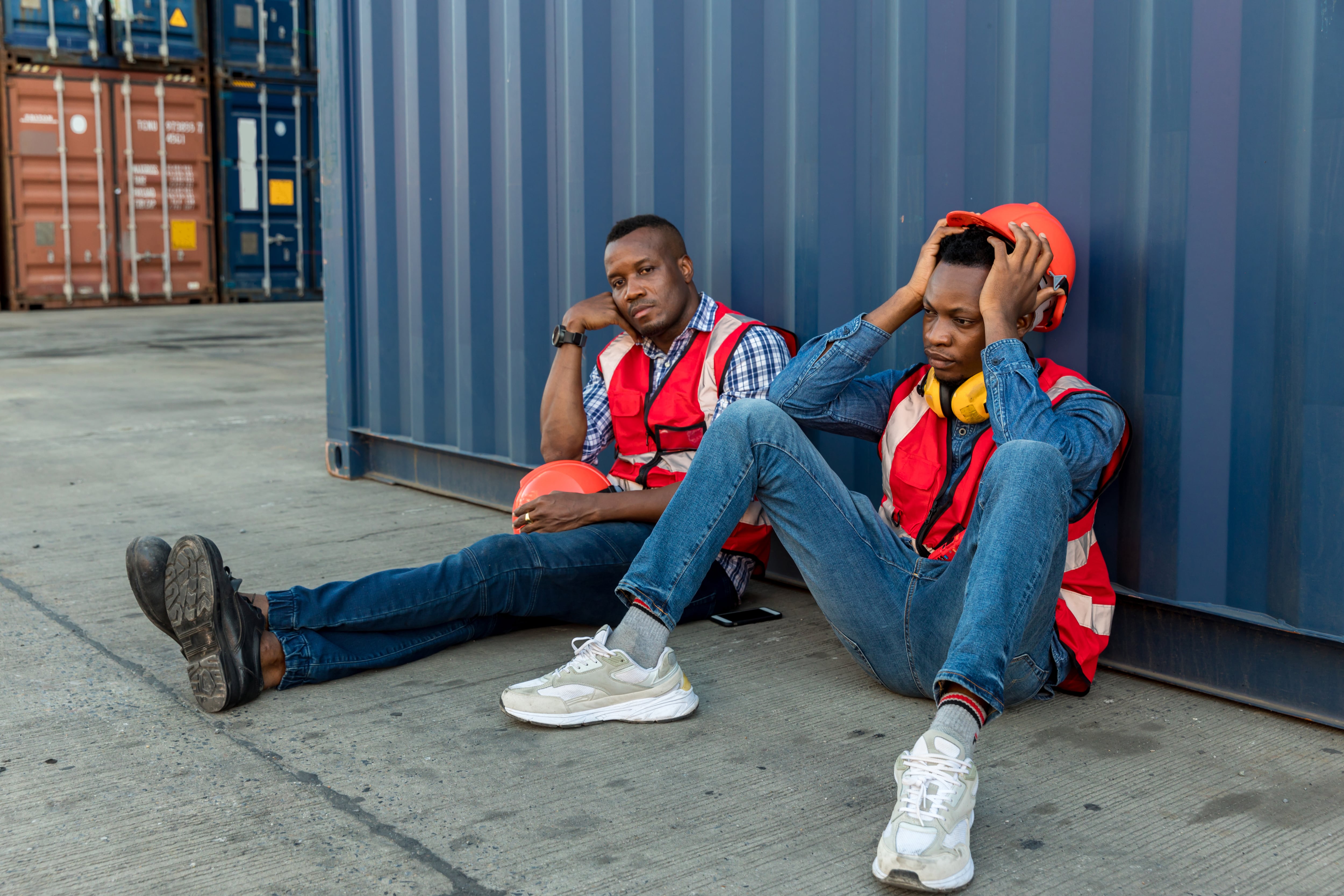 Un trabajador de fábrica se sienta cerca del contenedor de carga y parece cansado y ha perdido su empleo.