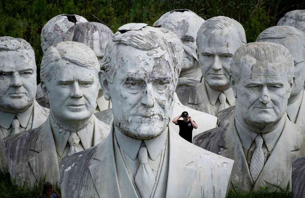 Un hombre ajusta su gorra mientras recorre el busto rescatado del presidente estadounidense Woodrow Wilson (al frente). 25 de agosto de 2019, en Williamsburg, Virginia. Howard Hankins rescató los bustos gigantes de ex presidentes de EE. UU. del parque de presidentes en Colonial Williamsburg cuando se le encargó destruirlos. (Foto por Brendan Smialowski / AFP)