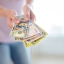 Primer plano de manos de mujer sosteniendo billetes de 50 mil pesos colombianos y 100 dólares