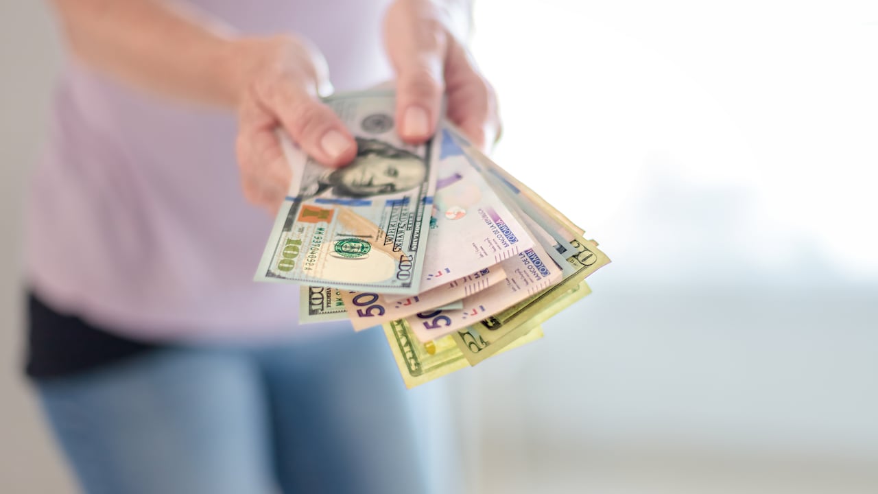 Primer plano de manos de mujer sosteniendo billetes de 50 mil pesos colombianos y 100 dólares