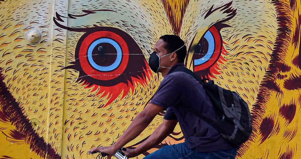 El colorido de las paredes parece contrastar con la expresión del hombre enmascarado en bicicleta. Cali, Valle del Cauca.