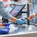 Mujer joven que paga con tarjeta de crédito de pase de pago en el lector de la caja registradora, empleada de ventas con máscara quirúrgica y guantes durante el brote de covid-19