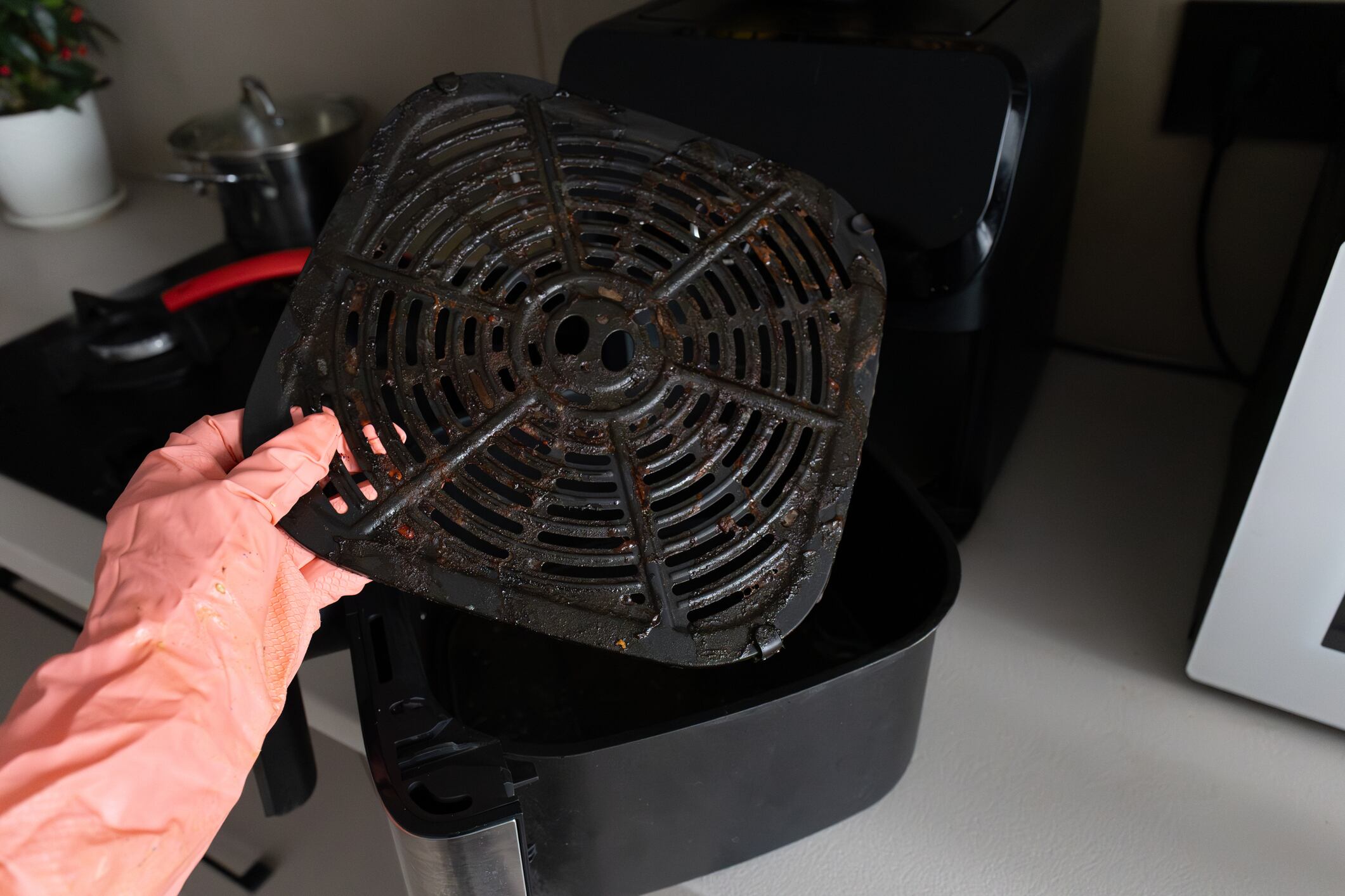 Manos con guantes de limpieza de goma rosa fregando y quitando la canasta sucia de la freidora de aire.