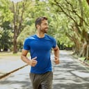 Hombre sonriente con auriculares para correr en el parque. El hombre adulto medio está escuchando música durante el verano. Lleva ropa deportiva.