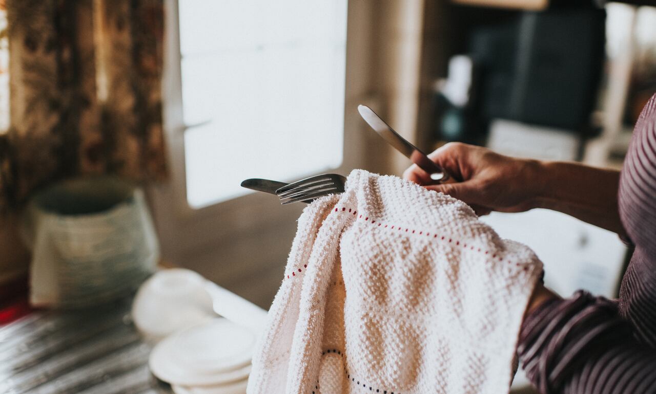 Woman in a kitchen with dish cloth, drying cutlery.