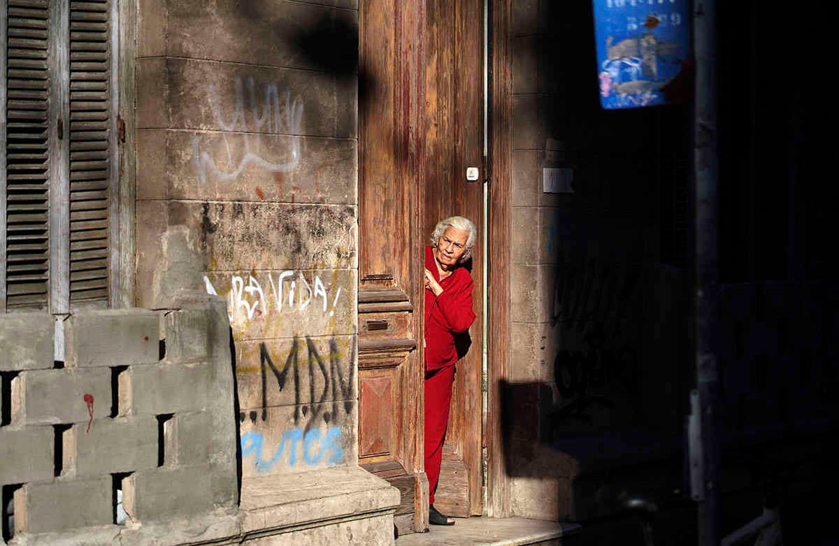 Una mujer mayor mira desde su puerta principal en Montevideo, Uruguay. (Foto AP / Matilde Campodonico)