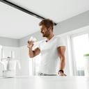 Nutrition Supplements. Handsome Happy Smiling Man With Muscular Body Drinking Protein Shake Before Workout. Sexy Athletic Fitness Male Model Enjoying Sports Drink Indoors. Bodybuilding, Healthy Eating