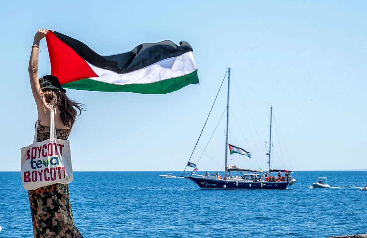 CATANIA, ITALY - JUNE 01: On the quay of San Giovanni Li Cuti, a woman raises the Palestinian flag shortly before the Madleen sets sail for Gaza on June 01, 2025 in Catania, Italy. Swedish activist Greta Thunberg is among those who will attempt to sail to Gaza on a boat organized by the Freedom Flotilla Coalition (FFC), in a bid to break Israel's blockade of the Palestinian territory. Freedom Flotilla had to abort a previous journey in early May after it said its boat came under attack by drones in international waters near Malta. (Photo by Fabrizio Villa/Getty Images)
