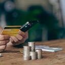 Close-up shot of Asian male hands holding bank card and smartphone. Use an app to shop online. Transfer money and pay with stacks of coins on the table.