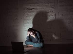 Sad and scared female Young woman with computer laptop suffering cyberbullying and harassment being online abused by stalker or gossip feeling desperate and humiliated in cyber bullying concept.